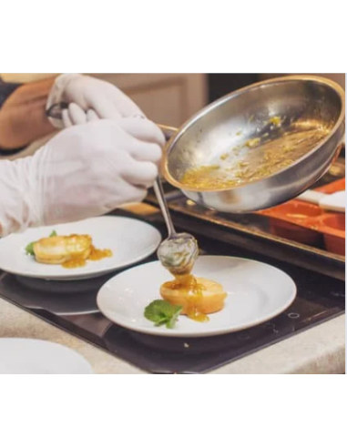 Kuhar z belimi nitrilnimi zaščitnimi rokavicami preliva omako na pripravljene jedi na belih krožnikih